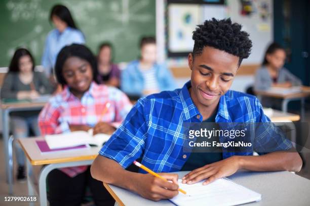 black ethnicity student writing while studying in classroom - high school stock pictures, royalty-free photos & images