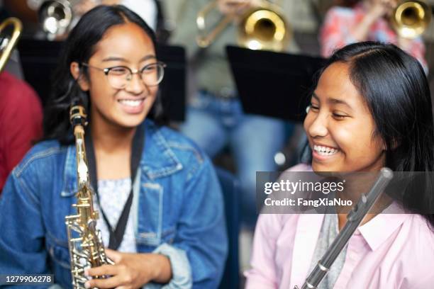 asian mixed race teenage female music students talking and laughing with brass instruments in class - teen musician stock pictures, royalty-free photos & images