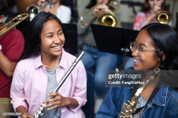 asian mixed race teenage female music students talking and laughing with brass instruments in class - orchestra rehearsal stock pictures, royalty-free photos & images