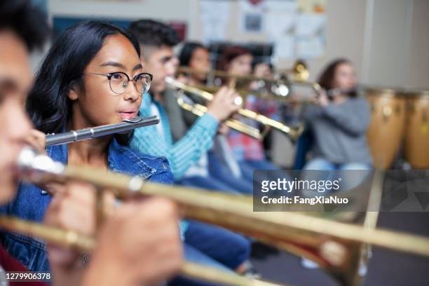 confident mixed ethnicity asian teenage girl playing flute in classroom during orchestra band class - orchestra rehearsal stock pictures, royalty-free photos & images