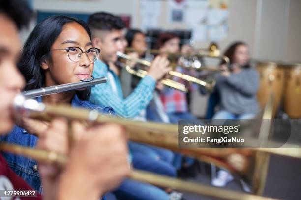 vertrouwen gemengde etnische etniciteit aziatische tiener die fluit in klaslokaal tijdens orkestbandklasse speelt - blaasinstrument stockfoto's en -beelden