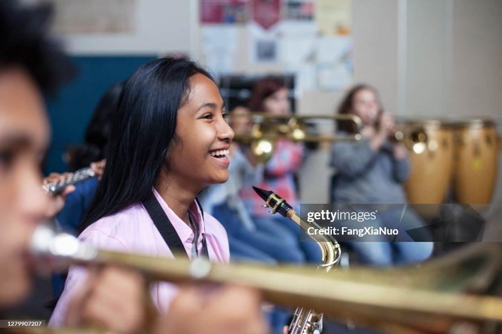 Alegre mixta etnia asiática chica asiática con saxofón en la clase de orquesta de banda