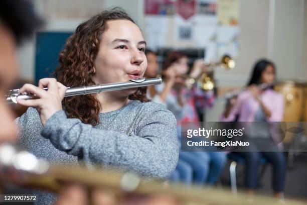 zuversichtliche weibliche brünette student üben flöte in band orchesterklasse - music band stock-fotos und bilder