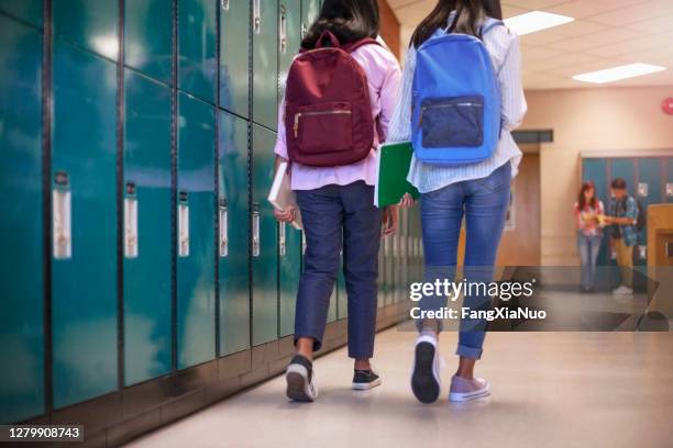 vrouwelijke klasgenootvrienden met rugzakken die door kluisjes op school lopen - brugklas stockfoto's en -beelden