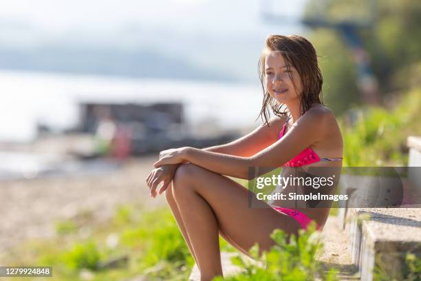 young slim teenage girl wears pink swimsuit and sits on a beach smiling, wearing braces. - kids swimsuit models stock pictures, royalty-free photos & images