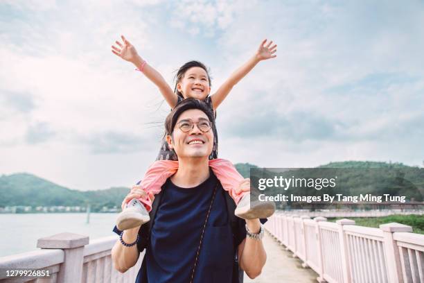 lovely little girl sitting on dad’s shoulders joyfully - llevar al hombro fotografías e imágenes de stock