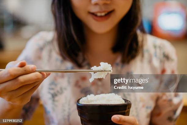 smiling young asian woman eating a bowl of white rice - rice bowl stock pictures, royalty-free photos & images