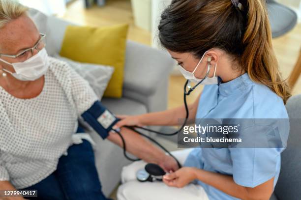 nurse measuring blood pressure of senior women at checkup meeting at home - altitude sickness stock pictures, royalty-free photos & images