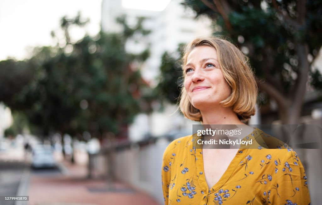 Smiling young woman looking up while standing on a city sidewalk