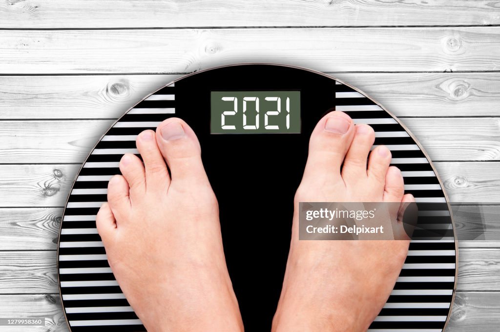 2021 feet on a weight scale on white planks, new year and holiday food nutrition and diet concept