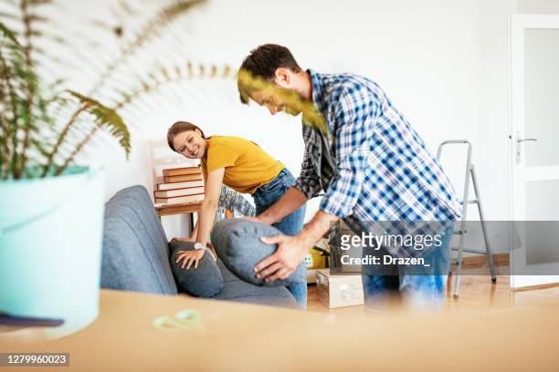 couple moving in new apartment, man and woman taking cover off the couch after moving in - new sofa stock pictures, royalty-free photos & images
