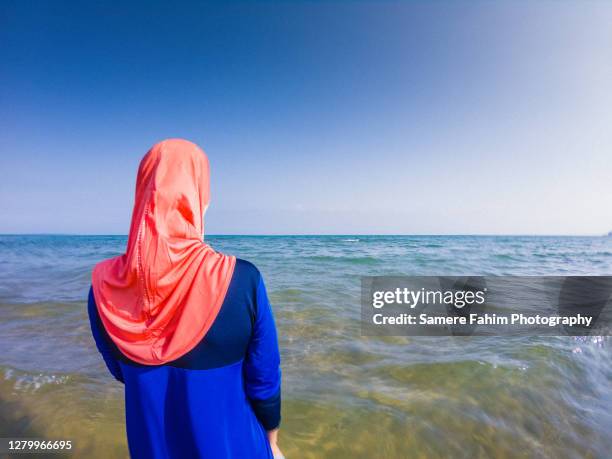 rear view of a muslim woman wearing a burkini on a beach - voile religieux photos et images de collection