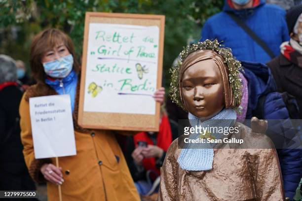Protester holds up a sign that reads: "Save the 'girl of peace' statue in Berlin" next to a memorial to World War II Korean "comfort women" at a...