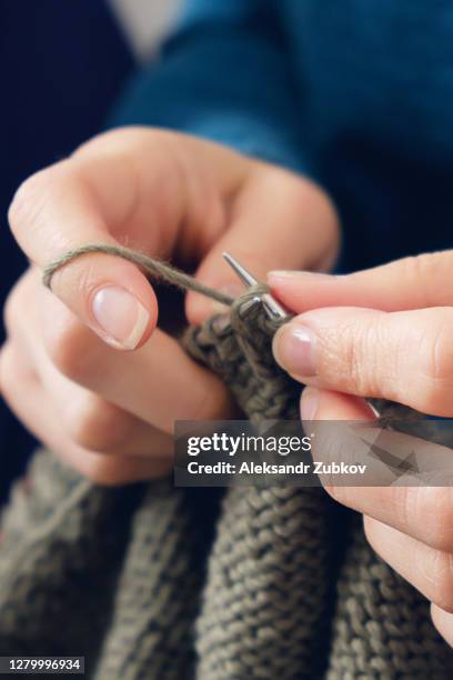 the girl is holding an unfinished knitting project and metal needles in close-up. a woman knits a dark green wool sweater. the concept of hobbies, creativity, needlework, handwork. - mani fili foto e immagini stock