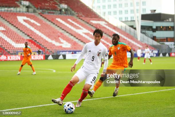 Daichi Kamada of Japan is challenged by Franck Kessie of Ivory Coast in front of empty seats during the international friendly match between Japan...