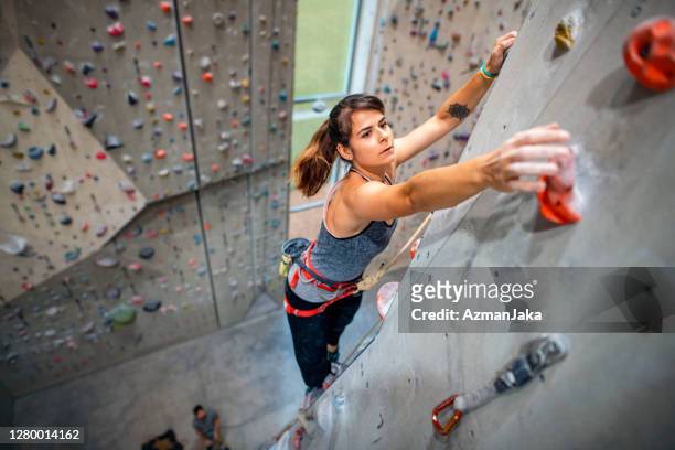 junge sportlerin, die nach handgriff auf kletterwand greift - indoor climbing stock-fotos und bilder