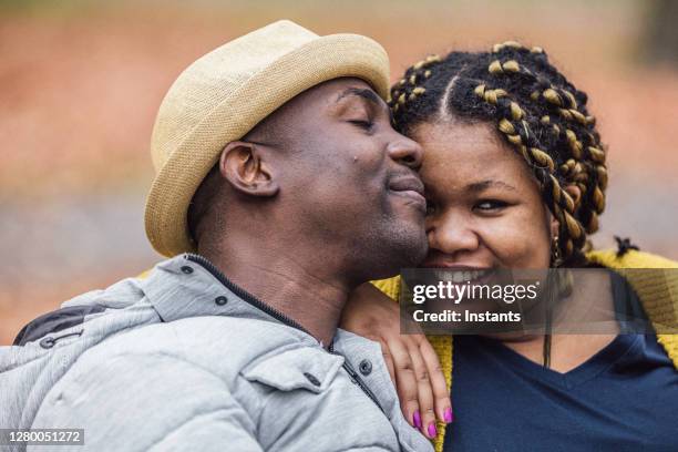 in a park, a happy and beautiful couple is enjoying a nice autumnal day while seated on a bench. - haitian ethnicity stock pictures, royalty-free photos & images