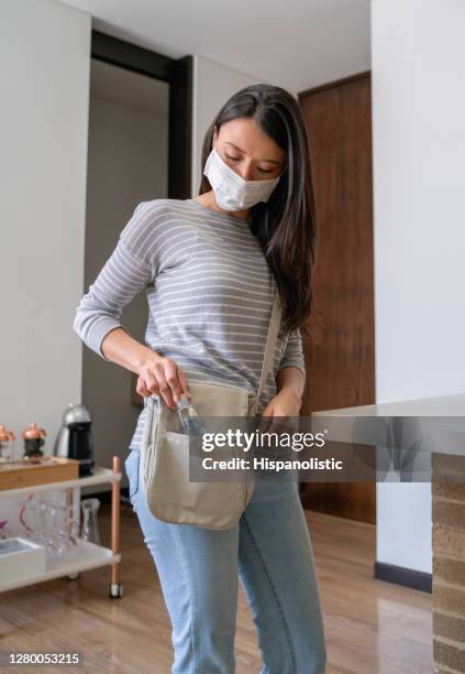 mulher usando uma máscara facial e colocando um desinfetante de mão em sua bolsa antes de sair de casa - hand sanitiser - fotografias e filmes do acervo