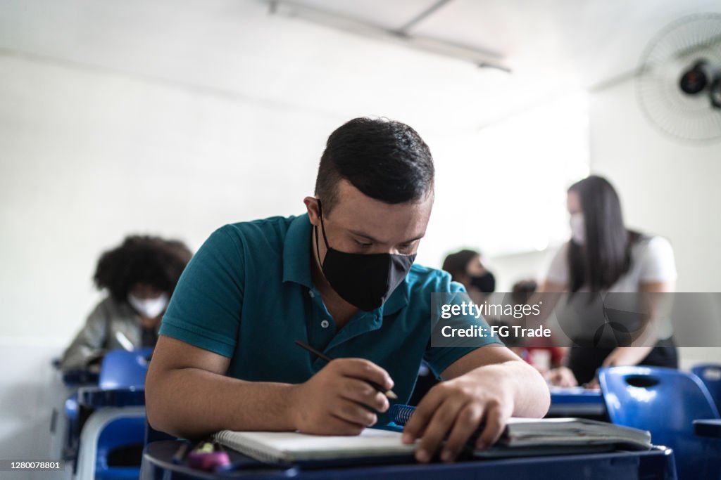 Estudiante universitario / de secundaria con síndrome de down usando mascarilla mientras estudia en el aula