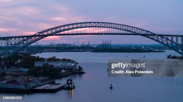 tugboats are moored in front of the bayonne bridge connecting new jersey, and new york state at sunset, with the remote view of the commercial docs and a port in the backdrop. - bayonne new jersey stock pictures, royalty-free photos & images