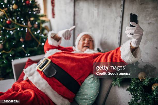 een kerstman die op de bank ligt en selfie met slimme telefoon maakt - santa claus lying stockfoto's en -beelden