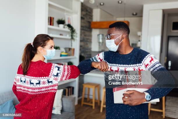 junge kaukasische frau begrüßt ihren afroamerikanischen freund in ihrem haus - coronavirus winter stock-fotos und bilder