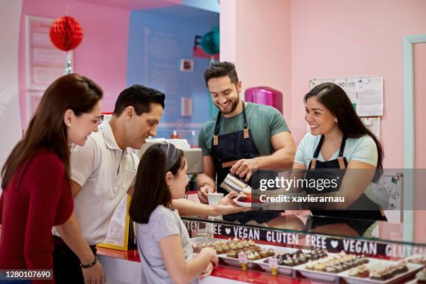 hispanic bakery staff serving cupcakes and coffee to family - small business saturday stock pictures, royalty-free photos & images