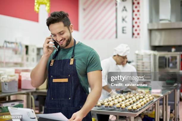 early 30s hispanic man using smart phone at bakery checkout - america patisserie stock pictures, royalty-free photos & images