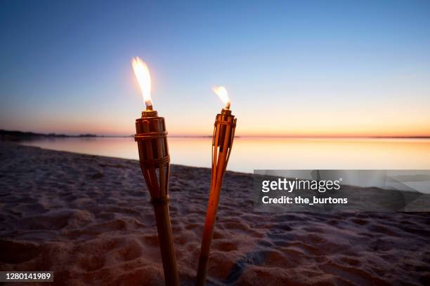 two burning torches in a bay of water by the sea at sunset - summer party lights stock-fotos und bilder