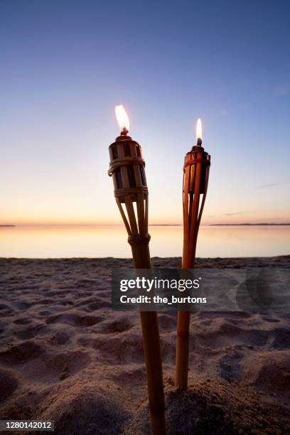 two burning torches on the beach at sunset - flaming torch stock pictures, royalty-free photos & images