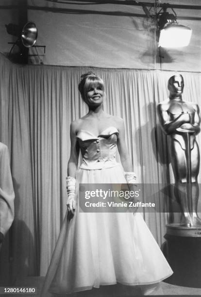 American actress Kim Basinger wearing a white strapless evening gown, with white evening gloves, attends the 63rd Annual Academy Awards, at Shrine...