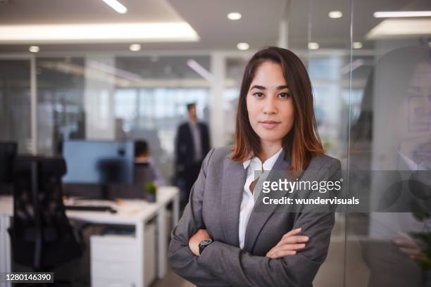 joven empresaria asiática apoyada en pared de cristal en la oficina moderna - vicepresident fotografías e imágenes de stock