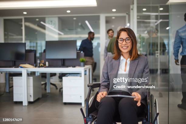 gehandicapte bedrijfsvrouw in rolstoelholdinglijst die in bureau glimlacht - wheelchair stockfoto's en -beelden