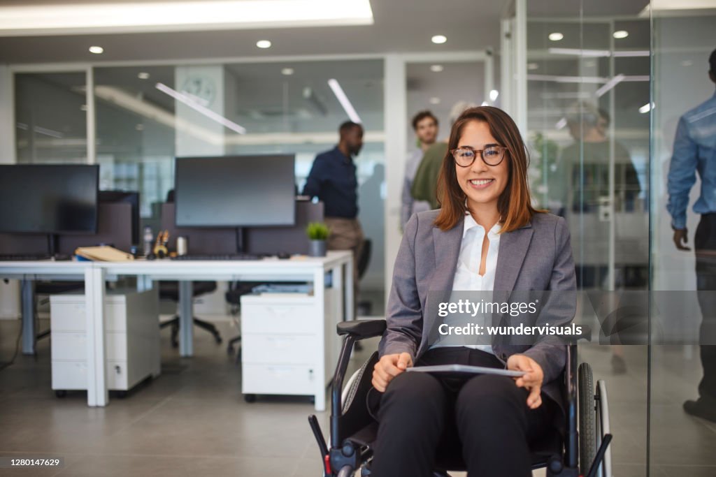 Disabled business woman in wheelchair holding table smiling in office