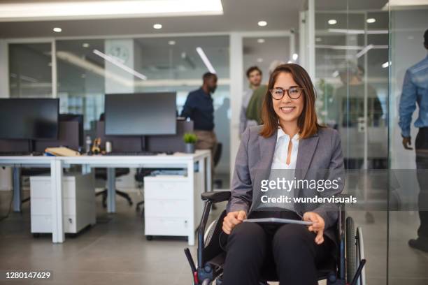 disabled business woman in wheelchair holding table smiling in office - disability stock pictures, royalty-free photos & images