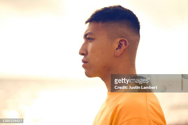 profile shot of a young man standing on a beach in a yellow t shirt - asain model men stock-fotos und bilder