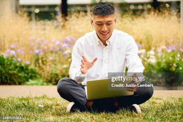 young man waving while on a video call on his laptop own the park - parc informatique bureau ordinateur photos et images de collection