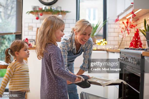 blond woman wearing blue apron and two girls standing in kitchen, baking christmas cookies. - kids cooking christmas photos et images de collection