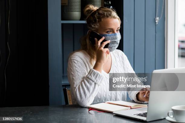 woman wearing face mask at a cafe table with a laptop computer, using mobile phone - watlington stock pictures, royalty-free photos & images