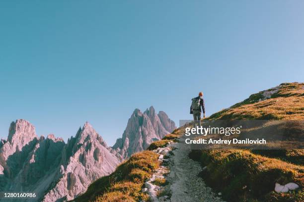 man hiking alone on the edge of the rock and looking towards the horizon. italian alps near the tre cime di lavaredo. - mountain stock pictures, royalty-free photos & images