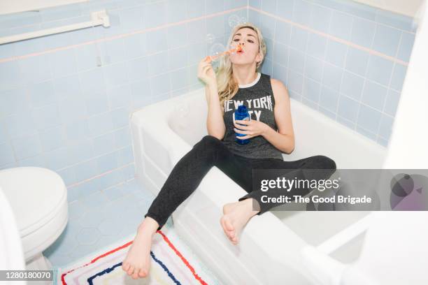 fully clothed young woman blowing bubbles in bathtub - fehl am platz stock-fotos und bilder