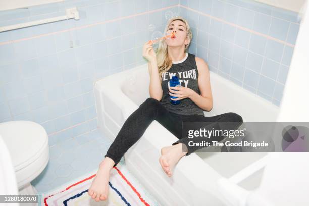 fully clothed young woman blowing bubbles in bathtub - generazione y foto e immagini stock