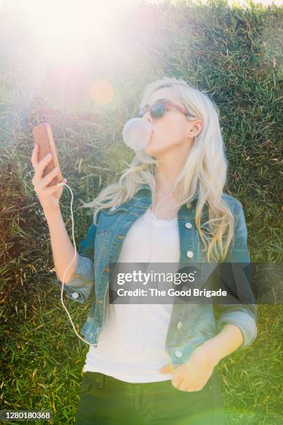 pretty woman standing outside taking a selfie while blowing a bubble - blonde woman selfie foto e immagini stock
