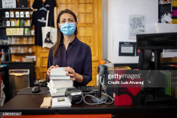 woman with face mask working at bookstore checkout - pile ou face stock-fotos und bilder