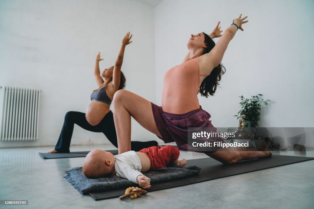 Two friends practicing yoga together, one of them is pregnant and the other one has a little child