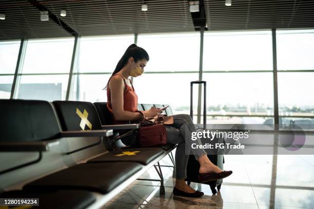 woman wearing face mask using smartphone in airport waiting area - airport mask stock pictures, royalty-free photos & images