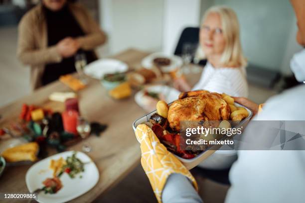 senior man serving food to friends at home - roast chicken table stock pictures, royalty-free photos & images