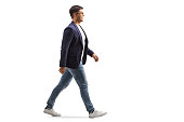 Full length profile shot of a smiling young man in jeans and suit walking