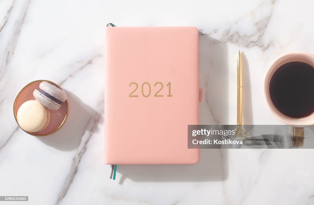 Roze koraal gekleurde dagboek voor het jaar 2021, pen, koffie, macaron cookie. Marmeren achtergrond