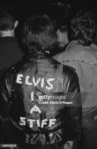 Member of the audience at a punk concert wearing a jacket with the phrase 'Elvis is a stiff' written on the back, circa 1977.